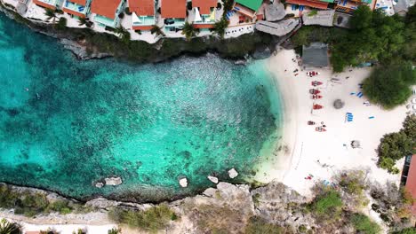 Die-Drohne-Fliegt-Von-Oben-Nach-Unten-über-Einen-Strand-In-Einer-Kleinen-Bucht-Und-Ein-Dorf-Auf-Curacao.-Luftaufnahmen-In-4K