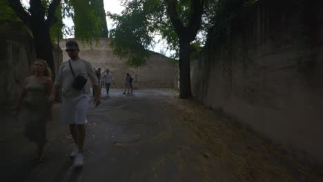 Punto-De-Vista-Inmersivo-En-Roma:-Moverse-Por-Calles-Concurridas-Hasta-Chiesa-Santi-Luca-E-Martina,-Italia,-Europa,-Caminar,-Tembloroso,-4k-|-Viajeros-Caminando-Por-Un-Camino-Oscuro-Cerca-De-La-Antigua-Puerta