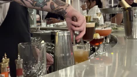 Close-Up-Bartender-Dropping-Large-Ice-Cube-Into-Drink-On-Busy-Bar