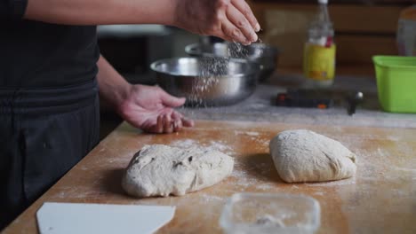 Dry-white-flour-sprinkled-over-wooden-tabletop-next-to-freshly-risen-dough,-filmed-as-medium-closeup-slow-motion-shot