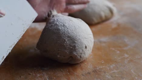 Puffy-ball-of-dough-shaped-and-shuffled-using-scraper-tool-on-wooden-kitchen-tabletop,-filmed-as-extreme-closeup-in-slow-motion-shot