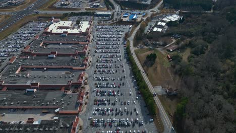Aerial-birds-eye-shot-of-full-parking-lot-at-shopping-center-in-America-and-driving-cars-on-highway