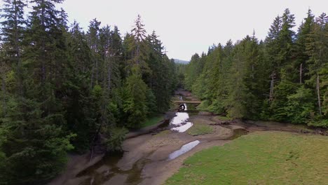 Woodland-Stream-with-Wooden-Bridge,-Calm-Aerial-Panning-Shot-in-Sandpit,-Canada