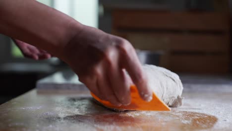 Freshly-risen-ball-of-sticky-dough-being-shaped-using-orange-scraping-tool-on-wooden-kitchen-tabletop,-filmed-as-close-up-in-slow-motion-style