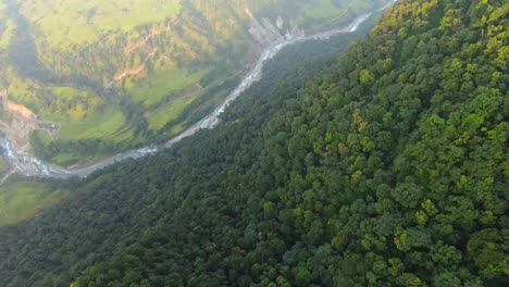 Aerial-top-down-shot-of-green-lush-mountains-and-flowing-river-in-the-valley-at-sunrise-in-Nepal