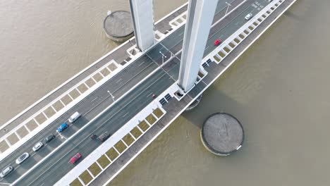Vehicle-traffic-crossing-the-Jacques-Chaban-Delmas-lift-bridge-over-the-Garonne-River-in-Bordeaux-France-to-Bassins-à-flots-neighborhood-,-Aerial-looking-down-tilt-up-shot