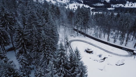Aerial-tilt-down-shot-of-forest-and-snowy-roads-in-Bavarian-mountains-during-winter-season,-Germany---Cars-driving-on-curvy-street