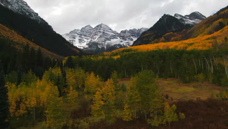 Colorful-Colorado-cinematic-aerial-drone-Aspen-Maroon-Bells-Capital-Peak-wilderness-14ers-autumn-fall-Aspen-Trees-first-snow-cloudy-morning-dramatic-incredible-landscape-backward-pan-up-reveal-motion