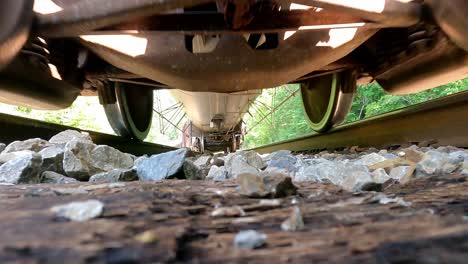 POV-under-the-moving-train-on-the-railway-tracks,-cargo-train-moving-on-top-of-the-railway-tracks-in-the-day