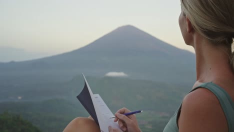 Mujer-Atractiva-Escribiendo-En-Un-Cuaderno-Mientras-Mira-Un-Inspirador-Paisaje-De-Montaña.