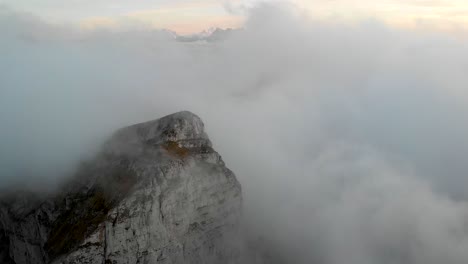Aerial-flyover-through-clouds-in-Leysin,-Vaud,-Switzerland-during-an-autumn-sunset-with-Dents-du-Midi-and-Tour-de-Mayen-in-the-view-and-with-hikers-on-Tour-d'Aï-waiting-for-clouds-to-disappear