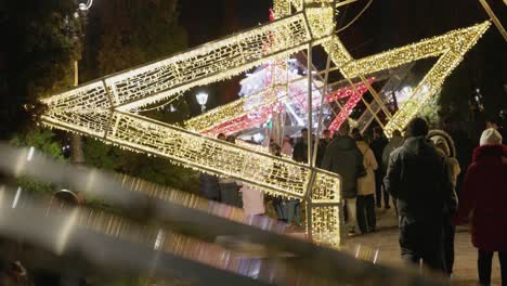 People-Strolling-Beneath-the-Grand-Star-Embellished-with-Vibrant-Lights-in-the-Park-as-Part-of-the-Galati-National-Day-Festivities-in-Romania---Medium-Shot