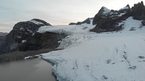 Aerial-flyover-over-the-glacial-lake,-ice-and-crevasses-of-the-Claridenfirn-glacier-in-Uri,-Swizerland-at-dusk