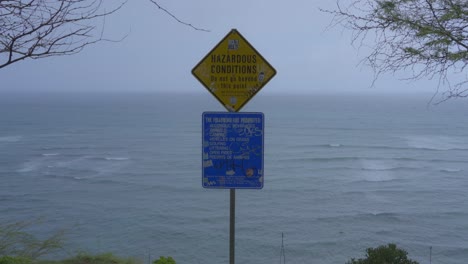 A-sign-warning-of-Hazardous-conditions-on-a-cliff-near-the-beach-in-Hawaii