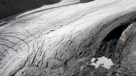 Aerial-flyover-over-the-Allalin-glacier-near-Saas-Fee-in-Valais,-Switzerland-with-a-pan-up-view-from-the-crevasses-and-ice-up-to-the-Rimpfischhorn-and-Strahlhorn-on-a-sunny-day-in-the-Swiss-Alps