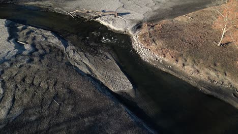 Drone-shot-of-a-pond-flow-that-is-badly-eroded-with-a-fallen-tree