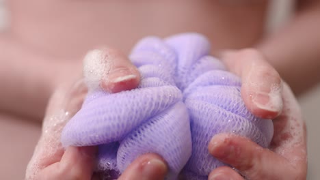 Purple-loofah-with-soap-in-woman's-hands,-closeup
