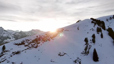 Sobrevuelo-Aéreo-Pendiente-Nevada-De-La-Montaña-Suiza-Y-Magnífico-Panorama-De-La-Cordillera-Con-Puesta-De-Sol-Dorada-En-El-Fondo