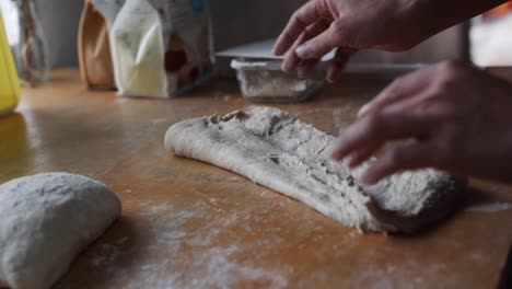 Freshly-stretched-dough-folded-in-preparation-for-kneading-on-wooden-kitchen-table-top,-filmed-as-closeup-slow-motion-shot
