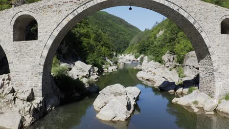 Retreating-drone-shot-revealing-the-arches-of-the-Devils-Bridgeand-the-Arda-River-located-in-Ardino,-at-the-foot-of-Rhodope-Mountains-in-Bulgaria