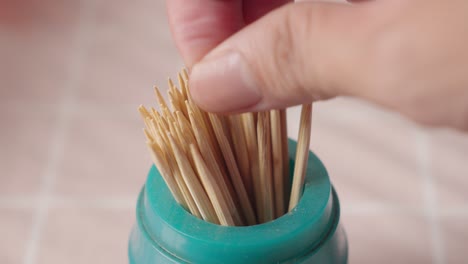 Hand-picking-up-a-wooden-toothpick-from-a-canister