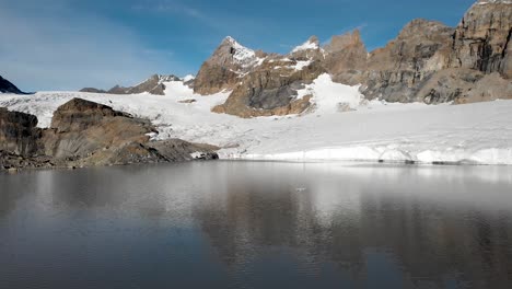 Sobrevuelo-Aéreo-Sobre-El-Agua-Y-Los-Icebergs-Del-Lago-Glacial-Hacia-El-Glaciar-Claridenfirn-En-Uri,-Suiza,-En-Una-Mañana-Tranquila-Y-Pacífica-Con-Picos-Alpinos-Detrás-De-Una-Pared-De-Hielo