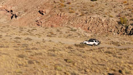 Kamerafahrt-Eines-Weißen-Geländewagens,-Der-An-Einem-Sonnigen-Tag-Auf-Einer-Unbefestigten-Straße-Durch-Die-Wüstenlandschaft-Von-Utah-Fährt