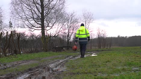 Man-in-yellow-safety-uniform-walk-away-near-muddy-private-property-dirt-road