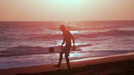 Silhouette-of-Young-Man-Playing-With-Soccer-Ball-on-Sany-Beat-at-Sunset,-Slow-Motion