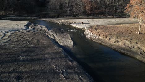 Backward-drone-view-of-a-pond-and-river-flow-that-is-badly-eroded-with-a-fallen-tree