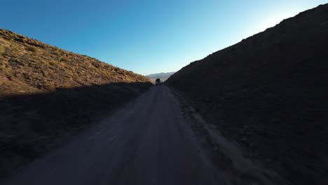 FPV-drone-zooms-towards-vehicle-driving-through-scenic-Utah-desert-hills