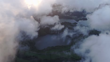 Flying-over-Lagoa-das-Sete-Cidades-lake-with-low-clouds-at-sunset,-aerial