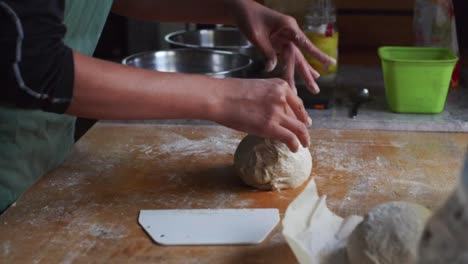 Fresh-dough-roll-being-plucked-by-hands-of-chef-on-kitchen-tabletop,-filmed-as-medium-closeup-slow-motion-shot