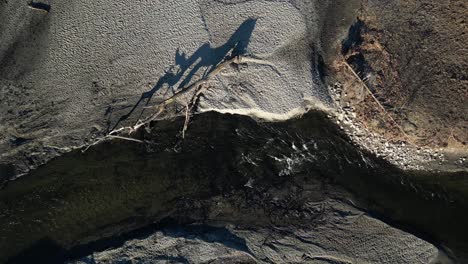 Drone-top-view-of-a-pond-and-river-flow-that-is-badly-eroded-with-a-fallen-tree