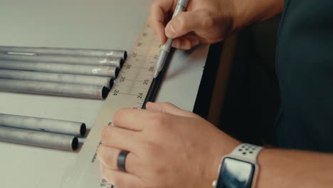 Male-hands-use-ruler-and-pen-to-measure-golf-club-shaft-length-for-custom-fitting-on-workshop-counter-in-slow-motion