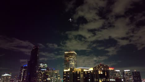 An-airplane-glides-above-Miami's-illuminated-downtown-skyline-in-the-evening,-enhancing-the-city's-vibrant-energy