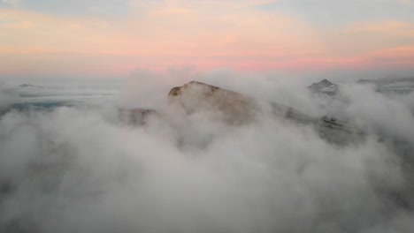 Aerial-flyover-through-clouds-in-Leysin,-Vaud,-Switzerland-during-a-colorful-autumn-sunset-with-hikers-on-Tour-d'Aï-enjoying-the-panoramic-view-above-clouds-with-Tour-de-Mayen-in-the-background