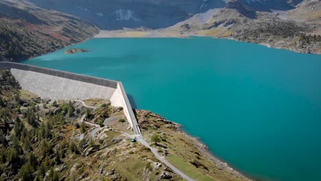 Aerial-view-of-Lac-de-Salanfe-and-its-hydroelectric-dam-in-Valais,-Switzerland-on-a-sunny-autumn-day-in-the-Swiss-Alps-with-a-pan-up-view-from-the-turquoise-waters-up-to-alpine-peaks-and-cliffs