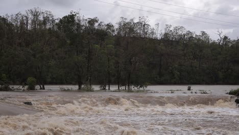 Coomera,-Gold-Coast,-2-January-2024---Trees-and-turbulent-water-across-the-Coomera-River-Causeway-under-flood-waters-from-the-2024-Storms-in-January