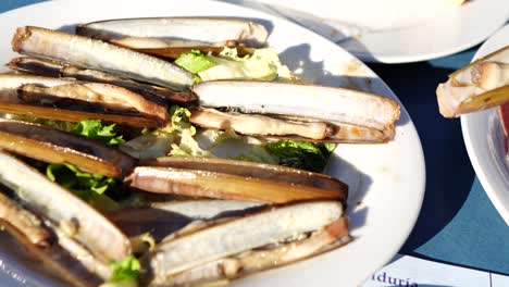 female-hand-taking-grilled-sea-clam-on-white-plate-with-lettuce