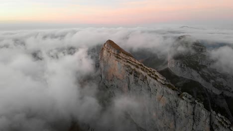 Aerial-view-of-Tour-d'Aï-in-Leysin,-Vaud,-Switzerland-during-a-colorful-autumn-sunset-with-hikers-and-climbers-enjoying-the-view-above-clouds-with-Tour-de-Mayen-in-the-background