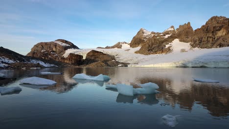 Peaceful-morning-scene-at-the-glacial-lake-next-to-Claridenfirn-glacier-in-Uri,-Swizerland-with-the-alpenglow-of-the-alpine-peaks-reflected-and-icebergs-floating-in-the-foreground