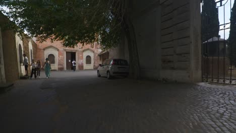 Rome-Immersive-POV:-Moving-In-Busy-Streets-to-Chiesa-Santi-Luca-e-Martina,-Italy,-Europe,-Walking,-Shaky,-4K-|-Family-Walking-In-Shadows-Near-Bright-Gate