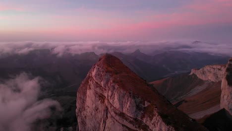 Aerial-flyover-around-Tour-d'Aï-in-Leysin,-Vaud,-Switzerland-during-a-colorful-autumn-sunset-with-hikers-and-climbers-enjoying-the-view-above-clouds-with-Tour-de-Mayen-in-the-background