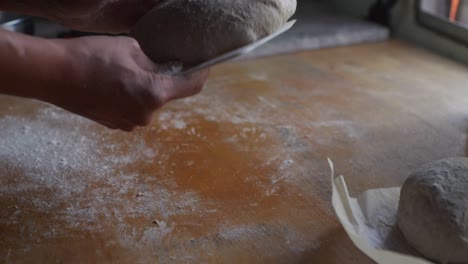 Freshly-kneaded-dough-flipped-over-on-wooden-kitchen-tabletop-using-white-plastic-scraping-tool,-filmed-as-closeup-shot-in-slow-motion-style