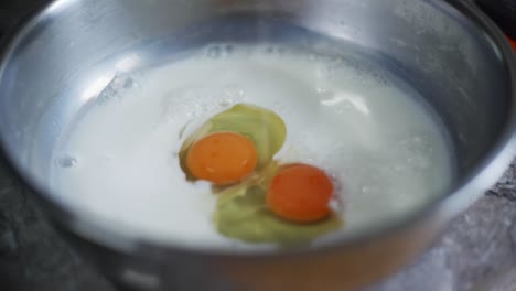 Freshly-cracked-egg-yolk-dropped-into-bowl-of-milk,-filmed-as-closeup-slow-motion-shot