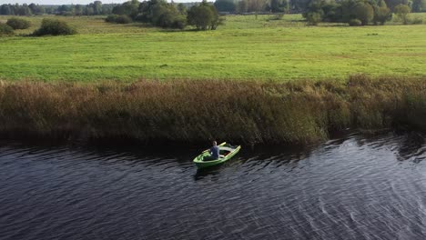 Circulating-drone-shot-with-man-on-fishing-boat-who-are-fishing-in-the-river-near-reeds