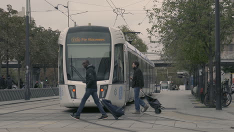 Tramway-Streetcar-Arriving-At-Station-While-People-Cross-Rails,-Porte-de-Vincennes-France