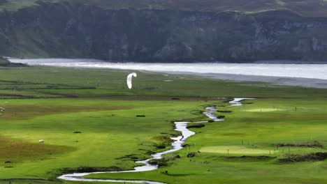 Kitesurfer-kiting-on-canal-through-lush-peat-bog-landscape,-Achill