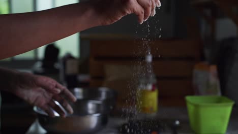Dry-white-flour-sprinkled-by-hand-directly-over-freshly-risen-dough-in-preparation-for-kneading-on-wooden-table-top,-filmed-as-closeup-slow-motion-shot